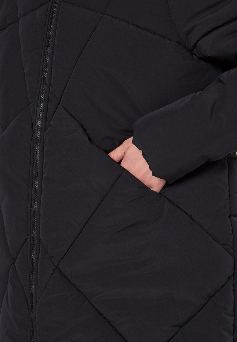 Schwarze Pufferjacke mit einem Rautenmuster, ausgestattet mit einem sichtbaren Reißverschluss und einer Hand in einer Seitentasche. Weiche, isolierte Textur.