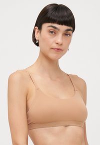 Lys beige trådløs bh med et glatt, elastisk stoff. Har brede skulderstropper og en enkel, sømløs design.