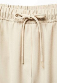 Pantalones de chándal beige con una cintura elástica y un cordón ajustable. La tela tiene una textura suave, con detalles en las costuras laterales.