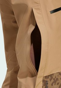 Smeđa jakna s dijagonalnom zatvaračnom džepom, glatkom teksturom i donjim dijelom s uzorkom u horizontalnim linijama tamnijih nijansi.