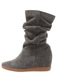 Stivale alla caviglia in suede grigio con design sdrucito, tacco a zeppa, punta affusolata e suola in gomma marrone a contrasto.