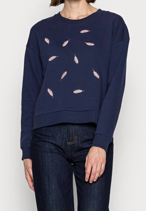 Navy blue long-sleeve sweatshirt with light pink feather designs scattered on the front, worn with dark blue jeans.