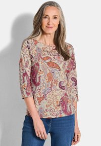 Langärmliges, gemustertes Oberteil mit einem floralen Paisleymuster in verschiedenen Orangetönen, Lila und Blau auf einem hellbeigen Hintergrund.