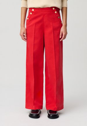 Pantaloni larghi rossi con pieghe frontali, caratterizzati da dettagli con bottoni dorati sui lati. Realizzati in un tessuto resistente, con una texture liscia.