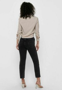Button-up shirt in light beige with fine stripes, black high-waisted jeans, and clear heeled sandals. The shirt has roll-up sleeves and a back yoke.