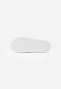 White sneaker sole with a textured rubber surface, featuring circular grip patterns and a rounded toe for enhanced traction.