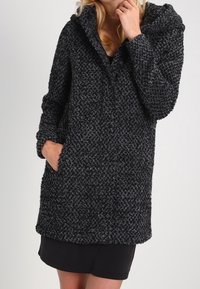 Svart och grå texturerad huoodiejacka med lös passform, framfickor och knäppning. Tyget har ett mönstrat mönster.