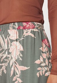 Jupe à motif floral avec une taille élastique, ornée de fleurs roses et bordeaux sur un fond vert pâle. Tissu doux et léger.