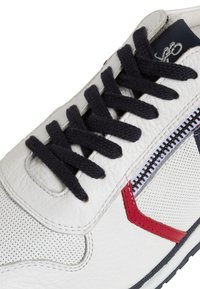 Fehér bőr sneaker fekete cipőfűzőkkel, piros és tengerészkék részletekkel és texturált felülettel. Oldalsó cipzárral rendelkezik.