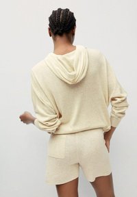 Felpa a maglia beige con vestibilità ampia e spalle scese, abbinata a pantaloni corti coordinati dotati di tasca posteriore. Texture liscia, aspetto morbido.