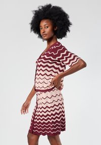 Knit dress set featuring a zigzag pattern in burgundy and soft pink. Short sleeves, V-neck, and ribbed accents at the waist and hem.
