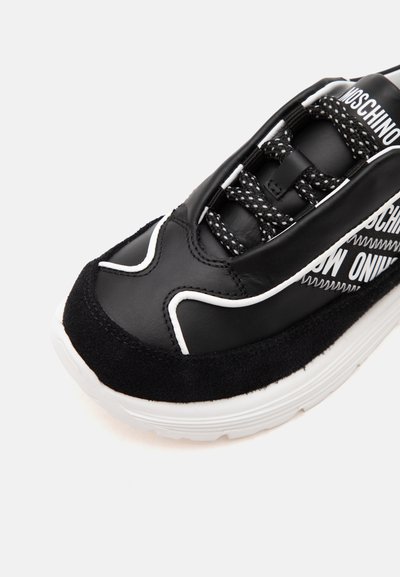 Baskets noir et blanc avec semelle texturée, lacets à motifs et détails en tissu marqué sur le côté et la languette.