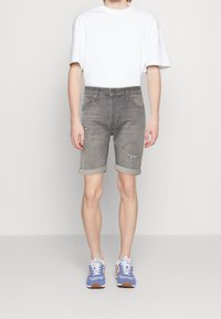 Shorts de denim gris con dobladillos enrollados, que presentan un diseño clásico de cinco bolsillos y detalles desgastados. Combinados con una camiseta blanca básica y zapatillas deportivas.