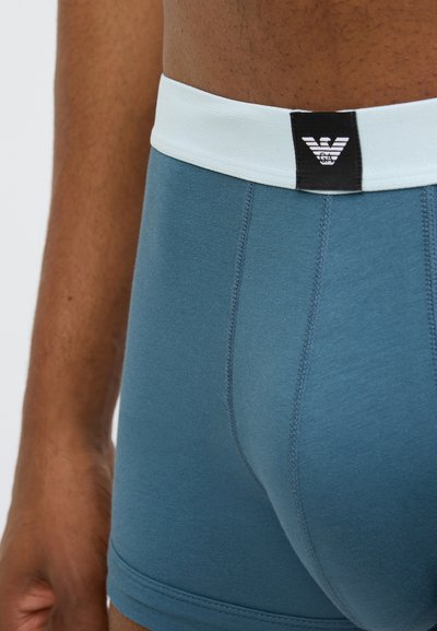 Mėlyni medvilniniai bokseriai su šviesiai mėlynu elastiniu juosmeniu ir juodu logotipo ženkleliu, pasižymintys plokščiomis siūlėmis patogumui ir aptakiu siluetu.