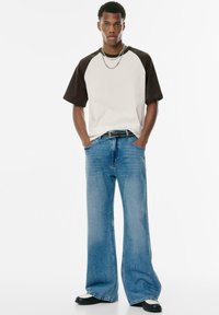Short-sleeve, cream and brown color-blocked T-shirt paired with light blue wide-leg jeans, accented with a black studded belt.
