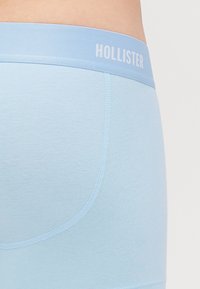 Boxeri de culoare albastru deschis, confecționați dintr-un material moale, cu un design ajustat și un elastic decorativ cu inscriptionarea "HOLLISTER" în litere albe.