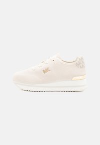 Light beige sneaker with a textured mesh upper, gold accents, a lace-up design, and a thick white sole with a serrated edge.