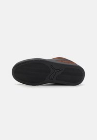 Brown suede sneaker with a textured black rubber sole, featuring a wavy pattern and a logo imprint. Design is low-profile with minimal accents.