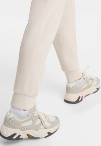 Light grey sneakers with a mix of suede and mesh, featuring white accents and a black sole. Worn with beige joggers.