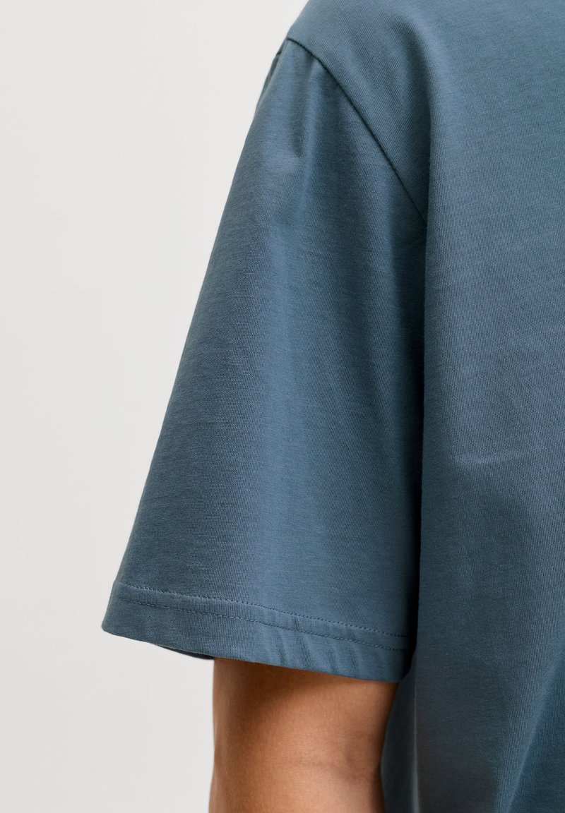 T-shirt a maniche corte realizzata in tessuto morbido e leggero di colore teal tenue; presenta una vestibilità rilassata con dettagli di cuciture sottili.