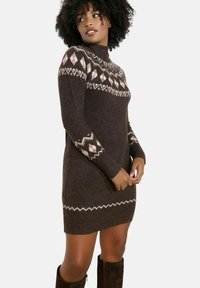 Abito maglione marrone con colletto alto, motivi geometrici in crema e beige, maniche lunghe e silhouette aderente, che termina a metà coscia.