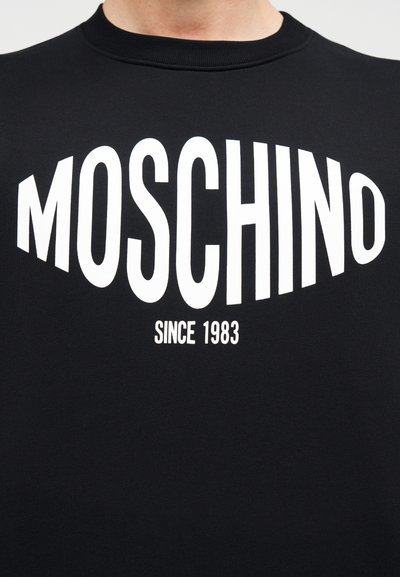 Μαύρο φούτερ με μεγάλο λευκό κείμενο «MOSCHINO» και «SINCE 1983». Στρογγυλή λ αιμόκοψη και απαλό ύφασμα με μεσαίο βάρος.