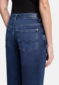 Ciemnoniebieskie dżinsy o wysokim stanie, z pięcioma kieszeniami i detalami stębnowania na tylnych kieszeniach. Teksturowany materiał z lekka elastycznością.