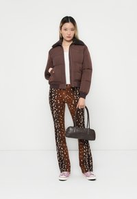 Giubbotto puffer marrone con colletto foderato in pelliccia, top bianco, pantaloni a zampa d'elefante marrone con motivo, e borsa nera; sneakers rosa e bianche.