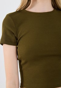 Oliivinvihreä lyhythihainen t-paita, joka on valmistettu ribbitetystä kankaasta ja jossa on pyöreä kaula-aukko. Struktuuroitu muotoilu parantaa näkyvyyttä.