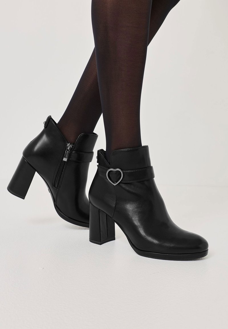 Bocanci negri din piele până la gleznă, cu vârful pătrat și toc gros. Dispune de un fermoar pe lateral și un accent în formă de inimă pe curea.