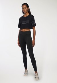 Czarna krótka koszulka z napisem "TRY TO", zestawiona z wysokim stanem czarnymi legginsami. Model nosi sneakersy z wielokolorowymi akcentami.