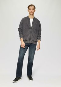 Grauer Reißverschluss-Hoodie mit gerippten Bündchen und Saum, kombiniert mit dunkelblauen Jeans und schwarzen Sneakers. Sanfte Textur, lässiges Design.