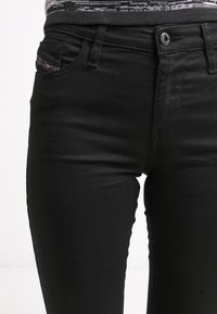 Vaqueros negros de denim con un ajuste ceñido, que cuentan con un bolsillo delantero, cierre con botón y detalles de costura sutiles. Textura suave y diseño elegante.