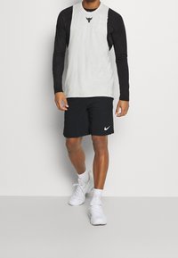 Jasnoszara bluzka bez rękawów z czarnym logo, w zestawie z czarnymi szortami z białym logo Nike i białymi sportowymi butami na sznurówki.