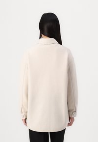 Beige wool blend oversized shirt jacket with a collar, long sleeves, button cuffs, and a curved hem, displayed from the back.