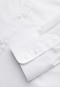 Chemise blanche habillée en gros plan montrant le poignet boutonné et les boutons avant sur un tissu lisse.