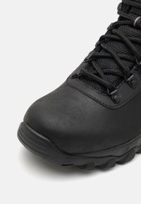 Botte de randonnée noire avec une tige en cuir texturé, semelle en caoutchouc et système de laçage sécurisé. Présente un bout arrondi et un talon renforcé.