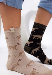 Beiga och svarta strumpor med leopardmönster; den beige strumpan har lejon i brunt, medan den svarta strumpan har lejon med en strukturerad mudddesign.