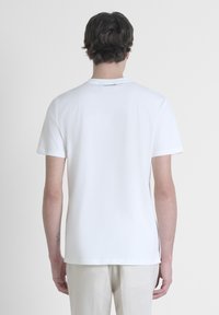 Camiseta blanca de manga corta hecha de algodón suave, con cuello redondo y un detalle de logo cerca del escote, que muestra un diseño simple.