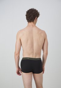 Schwarze Boxershorts mit grünem Bund, der das Logo "JACK & JONES" trägt, von hinten an einer Person mit kurzen, lockigen Haaren gezeigt.