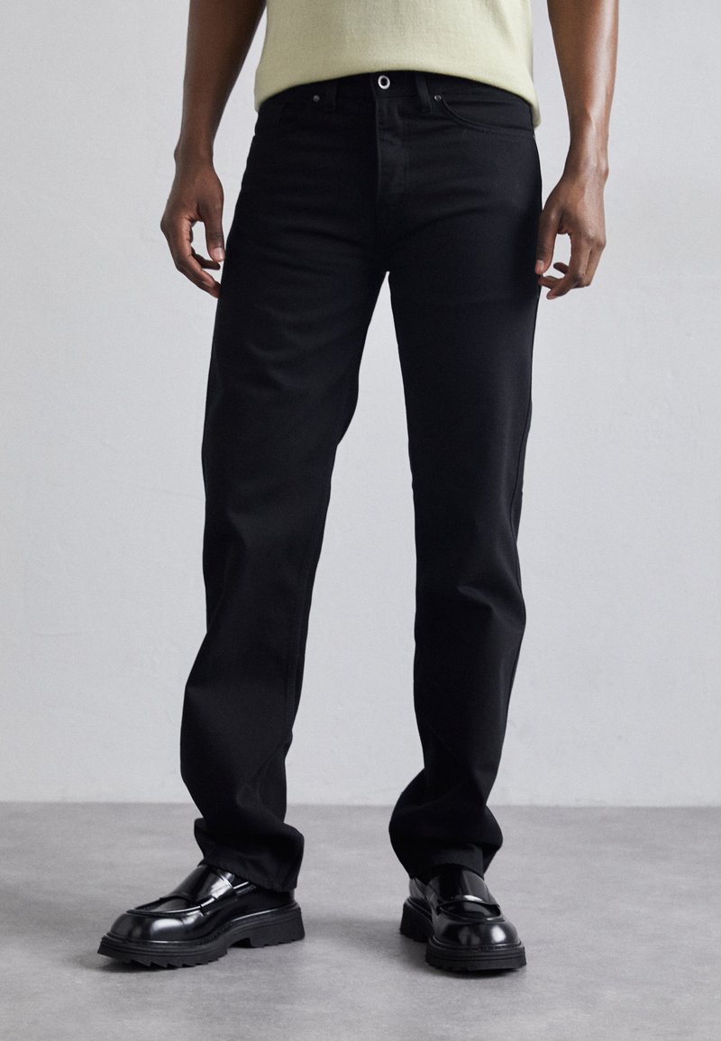 Svarta denimjeans med rak passform, featuring en klassisk femfickorsdesign och metallackenter. Slät textur, minimalistisk stil.