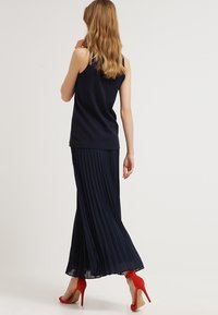 Marinblå plisserad maxikjol i kombination med en matchande ärmlös topp, kompletterad med klarröda högklackade skor. Slätt tyg och flödande design.