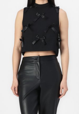 Crop top noir avec un col montant, en tissu texturé, et plusieurs nœuds en satin à l'avant. Associé à un pantalon en cuir noir taille haute.