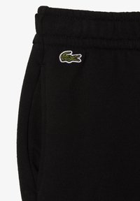 Schwarze Sweatpants aus weichem Stoff mit seitlichen Taschen und einem gestickten grünen Krokodil-Logo auf der oberen linken Seite.