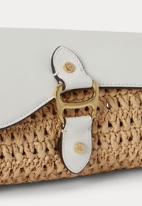 Baltos odos dirželis su auksine sagtimi ir vinutėmis prie pintos šiaudų tekstūros smėlio spalvos rankinės.