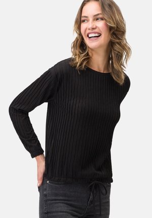 Maglietta nera a maniche lunghe con texture a coste, scollatura rotonda e dettaglio con cordoncino in vita, abbinata a jeans grigio scuro.