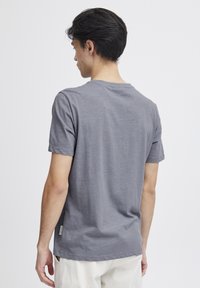 Tricou din bumbac gri, cu mâneci scurte și decolteu rotund. Textură netedă, detaliu de branding minim pe tivul lateral.
