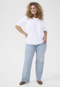 Camiseta blanca de manga corta con detalle de frente torcido, combinada con jeans rectos de mezclilla azul claro y zapatos planos marrones. Tejido suave y agradable al tacto.