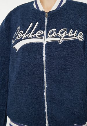 Marineblaue Fleece-Bomberjacke mit gerippten Bündchen und Saum. Mit "Kollege" in Weiß auf der Brust bestickt. Mit Reißverschluss.