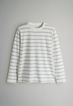 Ilgas rankovėmis baltas medvilninis marškinėlis su plonomis juodomis horizontaliosiomis juostelėmis, apvalia apykakle ir laisvo kirpimo, be matomų detalių ar akcentų.